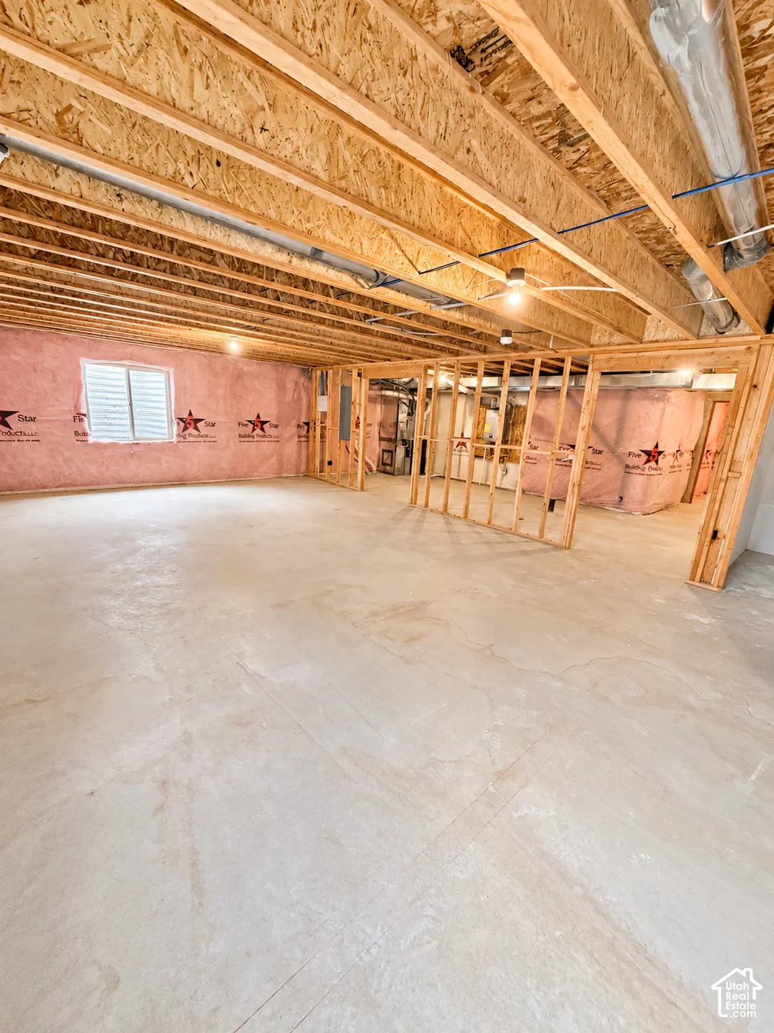 Unfinished lower level featuring concrete flooring, exposed wood ceiling joists, pink insulation-lined perimeter walls, and framed interior partition walls