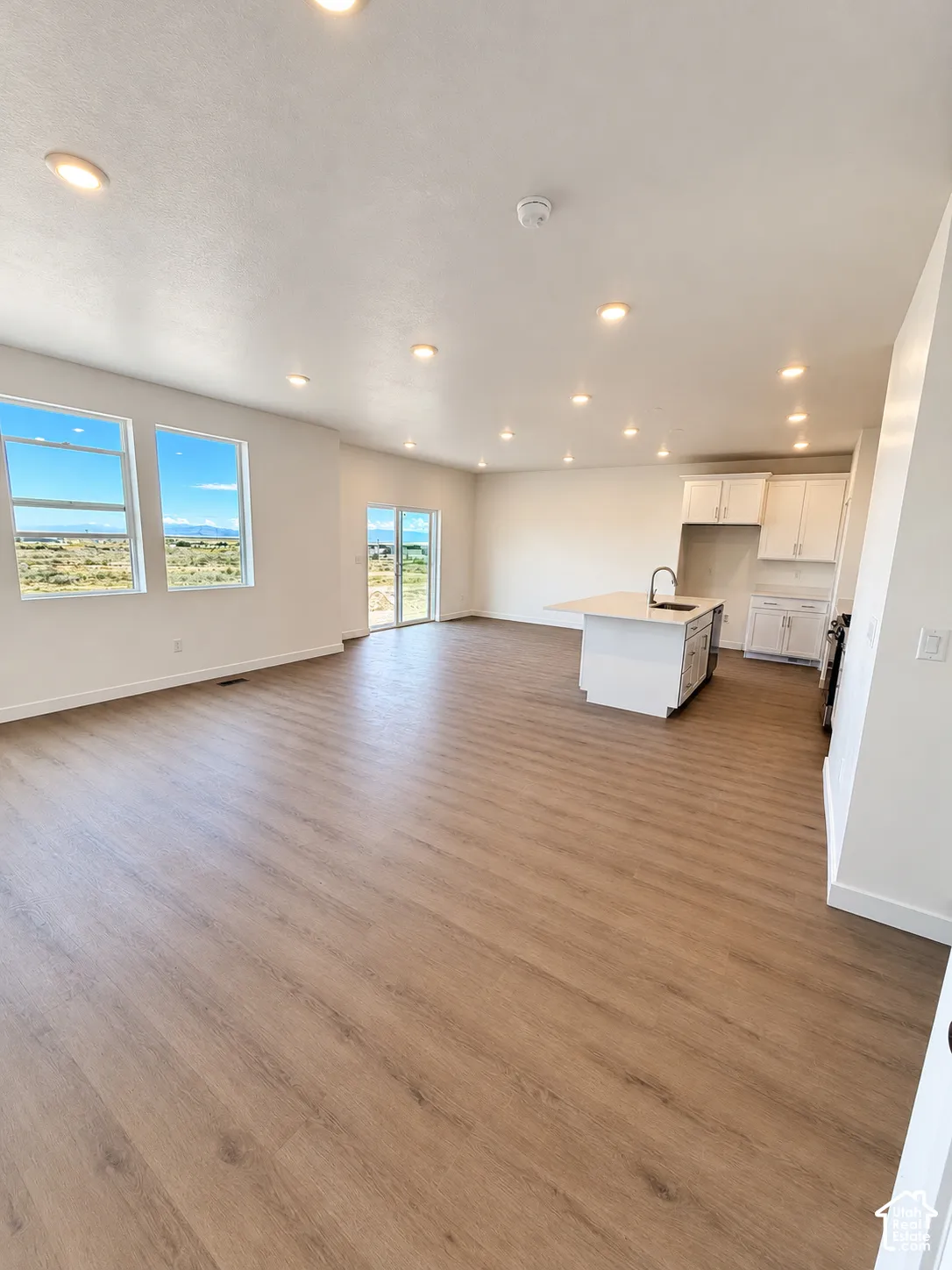 Open-concept interior featuring wood-finish flooring, recessed lighting, white cabinetry, a central kitchen island, and large windows providing natural light