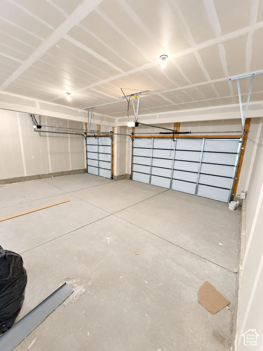 Three-car garage featuring drywall-finished walls, ceiling-mounted automatic door openers, and concrete flooring