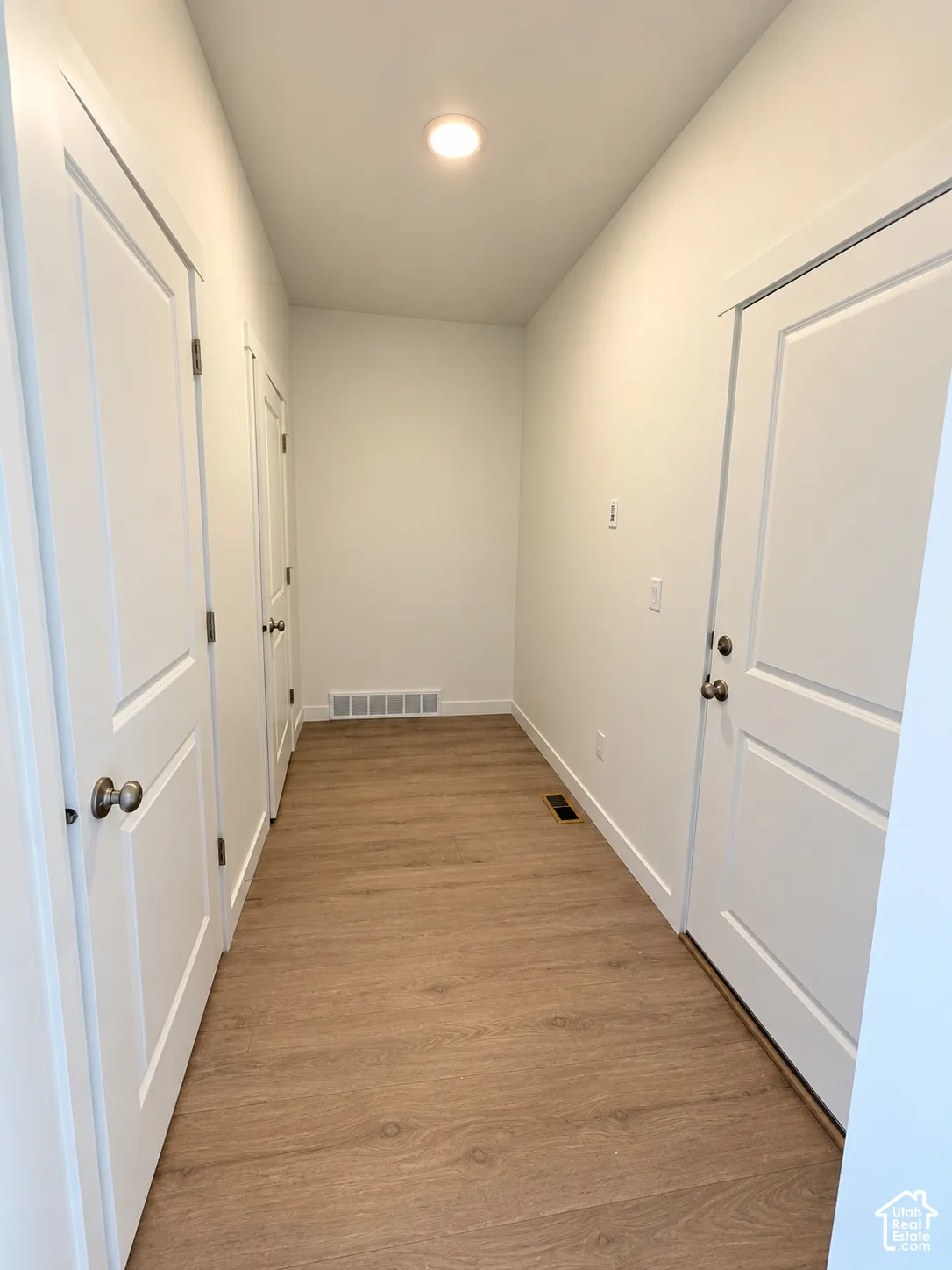 Hallway featuring wood-finish flooring, two-panel interior doors with satin nickel hardware, and recessed ceiling lighting