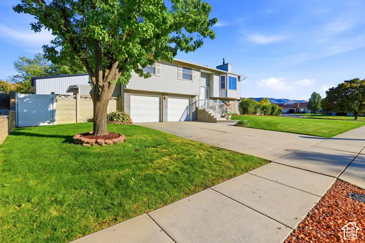 Split-level residence featuring a dual-car garage, horizontal siding, concrete driveway, and white privacy fencing