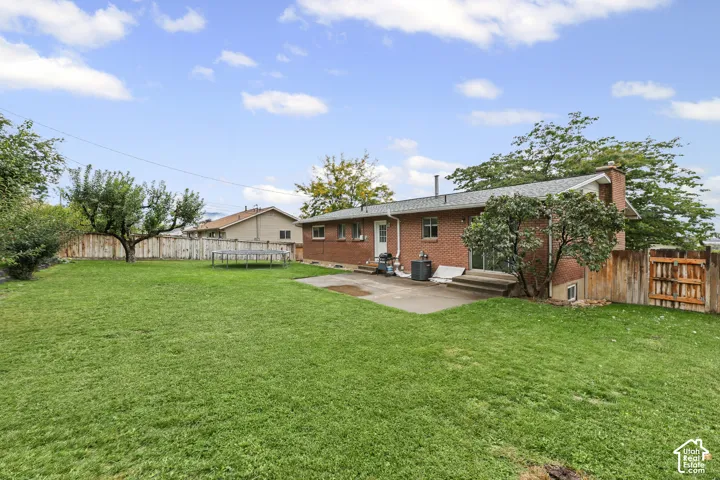 Spacious backyard featuring a brick exterior, concrete patio, mature trees, and wood fencing