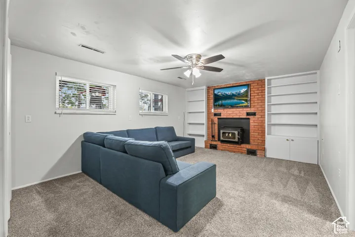 Red brick fireplace surround with an integrated hearth-mounted stove, flanked by floor-to-ceiling built-in shelving, complemented by a multi-blade ceiling fan