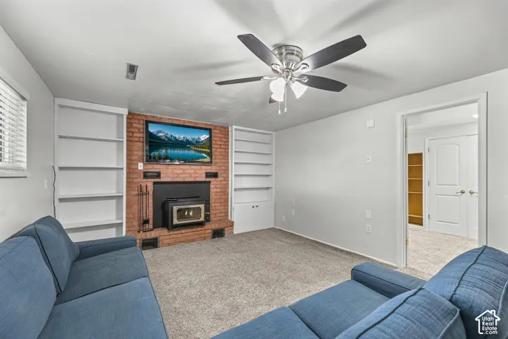 Exposed brick fireplace featuring a wood-burning stove insert, flanked by floor-to-ceiling built-in shelving, complemented by a multi-blade ceiling fan with integrated lighting