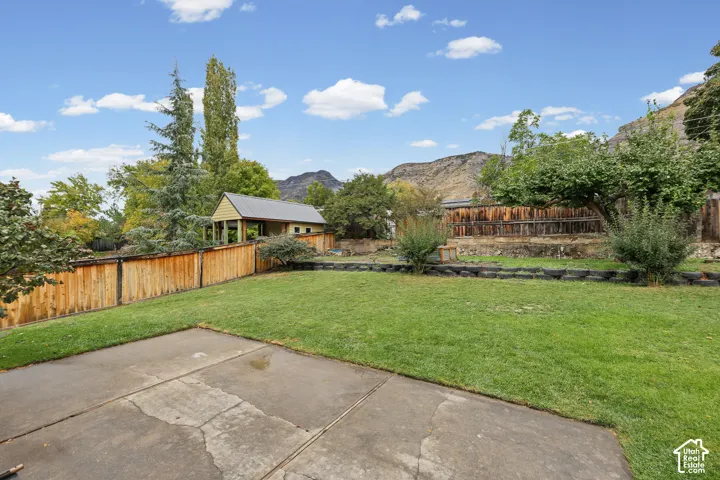 Backyard featuring a concrete patio, level lawn, wood privacy fencing, detached garage structure, and mountain backdrop