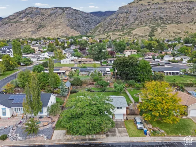 Aerial perspective showcasing a residential property featuring solar panels, a two-car garage, mature landscaping, and an expansive mountain backdrop