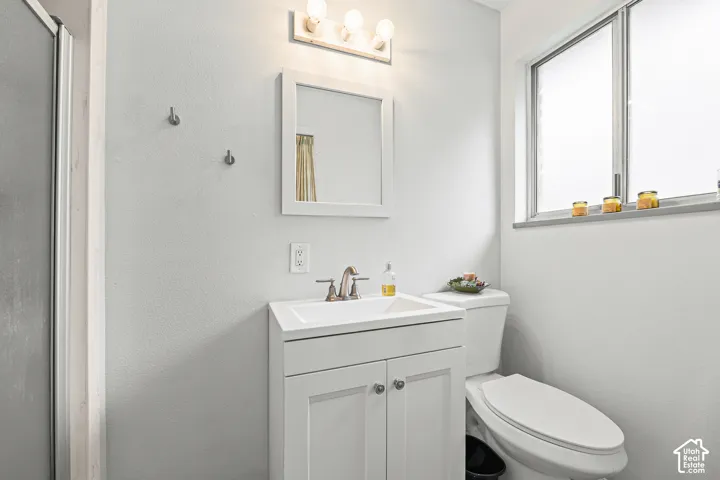 White vanity featuring an integrated sink with a metal faucet, framed wall mirror, three-bulb vanity light fixture, and large window with natural light