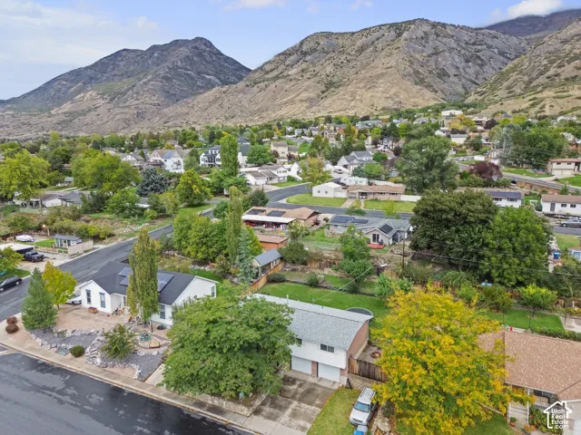 Aerial perspective showcasing a residential lot featuring mature trees, landscaped stone elements, a multi-level structure with a two-car garage, and prominent mountain backdrops