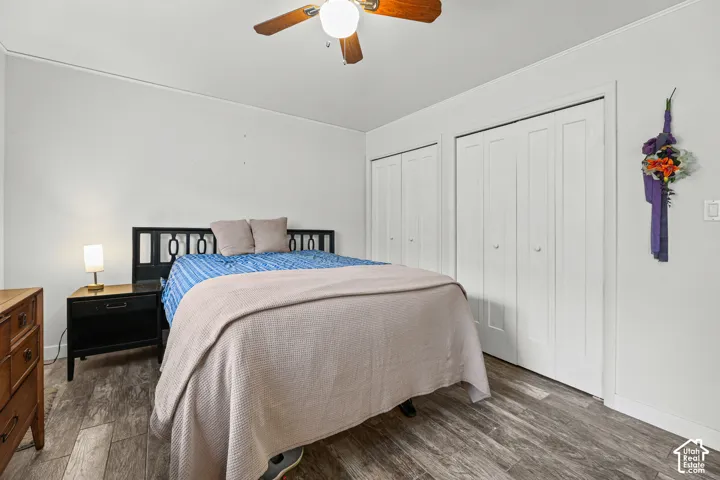 Bedroom featuring wood-finish flooring, dual bi-fold closets, and a ceiling fan with light fixture