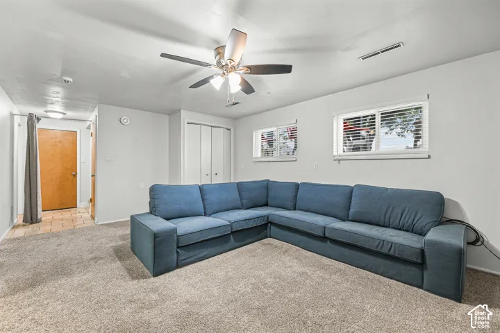 Neutral-toned room featuring wall-to-wall carpeting, dual windows, a ceiling fan with integrated lighting, and a built-in closet with sliding doors