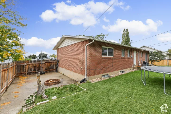 Exterior featuring red brick construction, concrete patio, perimeter wood fencing, and a manicured lawn