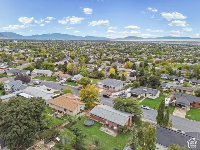 Aerial perspective showcasing a residential property featuring a large backyard, mature trees, an asphalt driveway, and a distant mountain backdrop