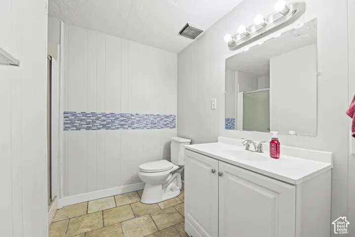 Bathroom featuring a white vanity cabinet, integrated sink with a chrome faucet, wall-mounted mirror, four-light vanity fixture, and stone-tile flooring with decorative mosaic tile accent detailing