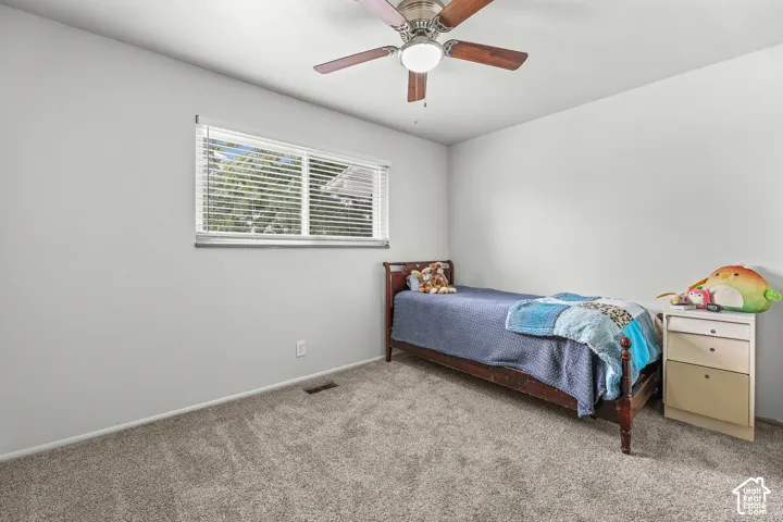 Neutral-toned carpeting, ceiling-mounted fan with integrated lighting, and horizontal window blinds