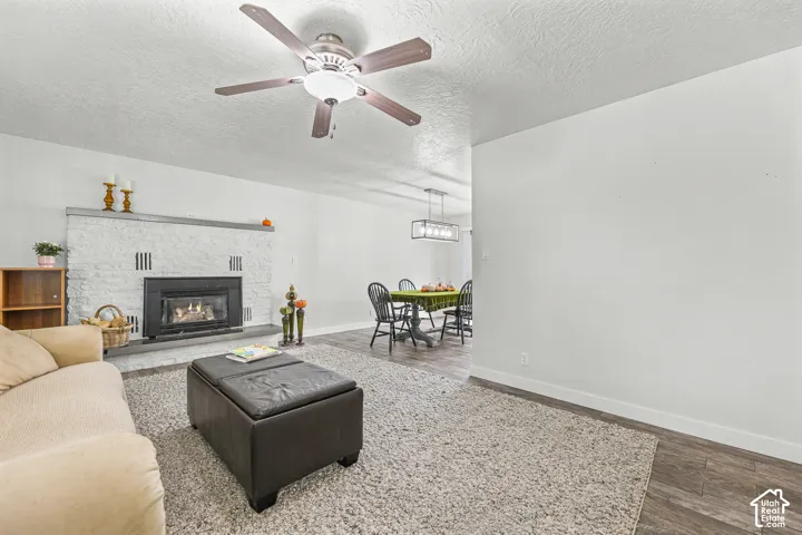 Textured white masonry fireplace with a fireplace insert, wood-finish flooring, ceiling fan with integrated lighting, and a linear pendant light fixture