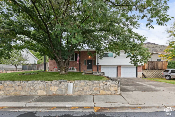 Split-level residence featuring a brick and horizontal siding facade, a double-car garage, and a stacked-stone retaining wall with an elevated lawn and mature tree