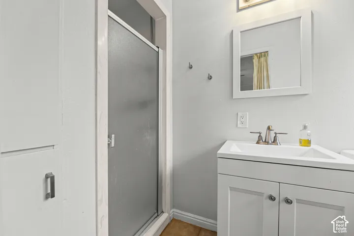 Bathroom featuring a white vanity cabinet with a integrated sink, polished metal faucet, matching framed mirror, built-in cabinetry, and a shower stall with a frosted glass door