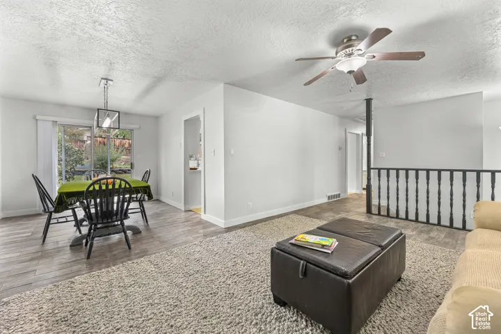 Living area featuring wood-finish flooring, ceiling fan with light kit, pendant lighting, and a metal stair railing