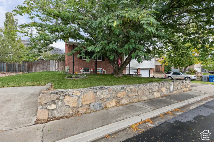 Exterior facade featuring red brick masonry, white horizontal siding, a terraced natural stone retaining wall, and mature shade trees