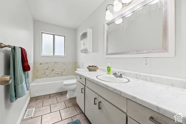 Bathroom featuring a long vanity with a stone-patterned countertop, integrated basin, wall-mounted storage cabinet, large framed mirror, and tile flooring