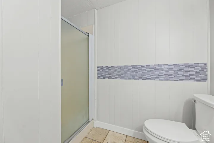Shower enclosure with a glass door, paneled walls with tile accents, and stone-finish floor tile