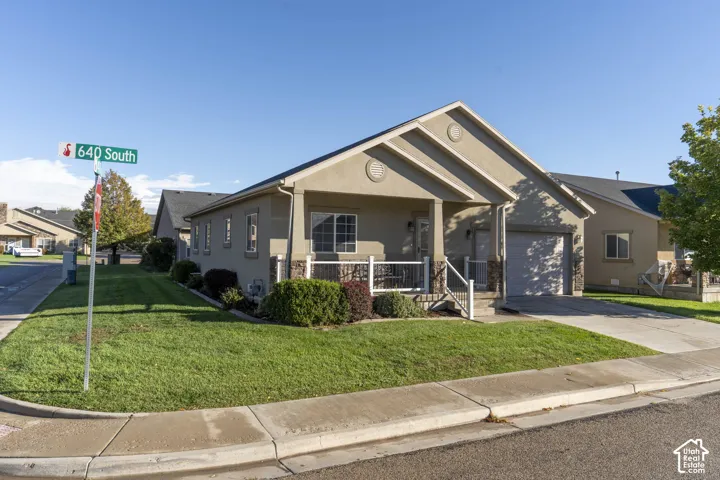 Stucco exterior featuring a covered front porch with stone-accented columns, white railing, a concrete driveway, and a two-car garage