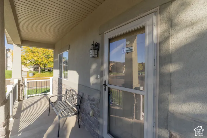 Covered front porch featuring concrete flooring, stone veneer siding, metal railing, and wall-mounted exterior lantern lighting