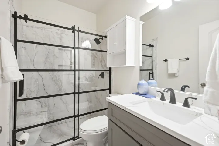 Shower with a black metal grid-frame sliding door, stone-pattern wall tile, built-in storage cabinet, hard surface countertop with integrated sink, and matte black fixtures