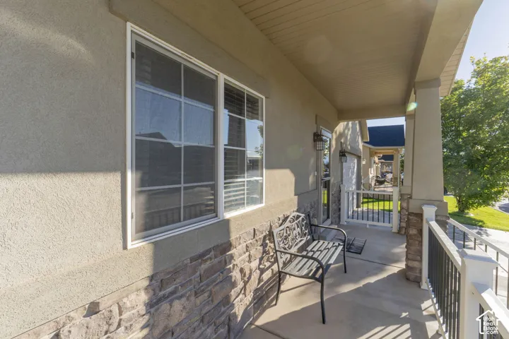 Covered front porch featuring stone veneer siding, concrete flooring, decorative column accents, and iron-style railings