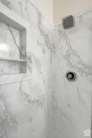 Shower surround featuring veined stone-look tile, built-in recessed wall niche, wall-mounted rain shower head, and single-handle pressure balance valve