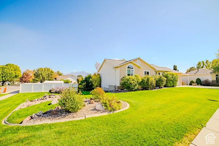 Single-story residence featuring light-toned siding, a decorative arched window, manicured lawn, xeriscaped rock garden with mature shrubbery, and mountain backdrop