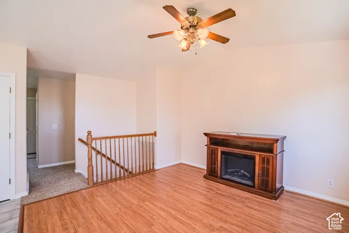Wood-finish flooring, vaulted ceiling with a multi-light ceiling fan, and wooden stair railing