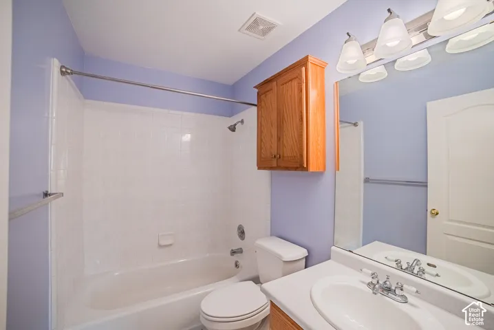 Full bathroom featuring a tub-shower combination with white tile surround, wall-mounted wood cabinetry, a vanity with an integrated sink, and a large vanity mirror with multi-bulb light fixture