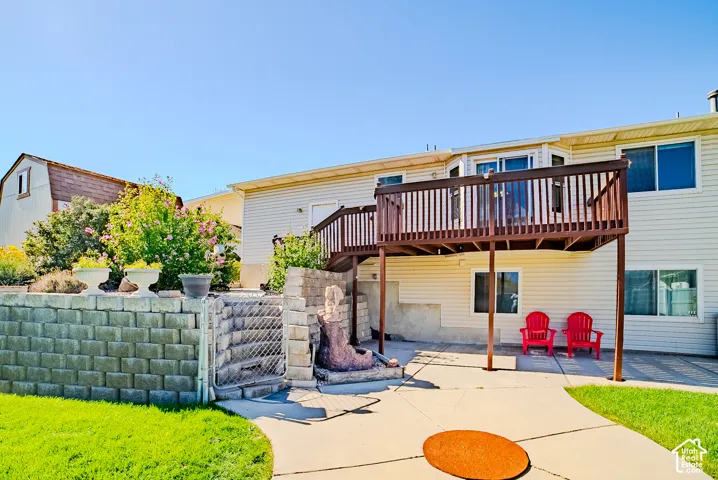 Exterior space featuring a raised wooden deck with railings, concrete patio, tiered stone retaining wall, and fenced landscaping