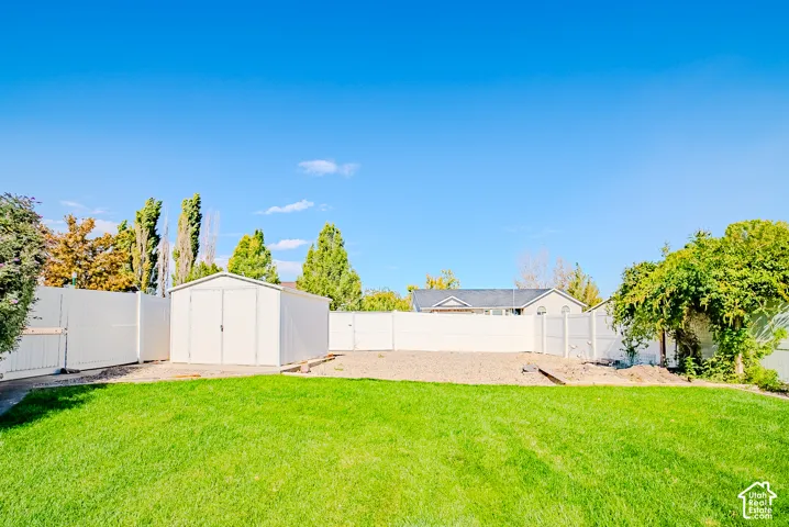Backyard featuring a manicured lawn, gravel ground cover, white vinyl perimeter fencing, and a detached storage shed