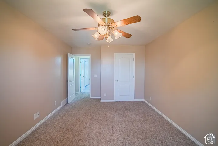 Neutral-toned interior featuring wall-to-wall carpeting, a multi-blade ceiling fan with integrated lighting, and white paneled doors