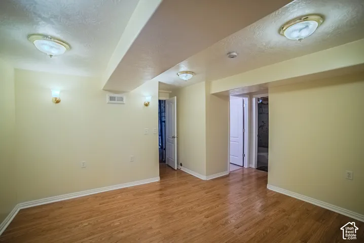 Interior space featuring wood-finish flooring, textured ceiling, multiple flush-mount light fixtures, and wall-mounted sconce lighting