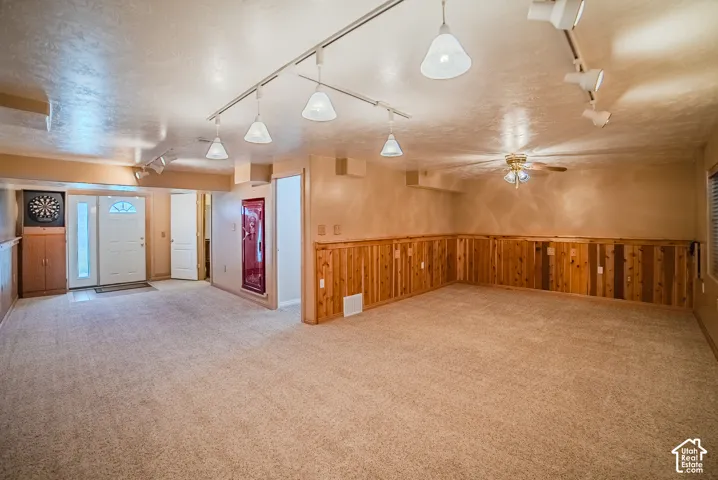Expansive interior room featuring wall-to-wall carpeting, wood panel wainscoting, track lighting, ceiling fan, and a built-in safe