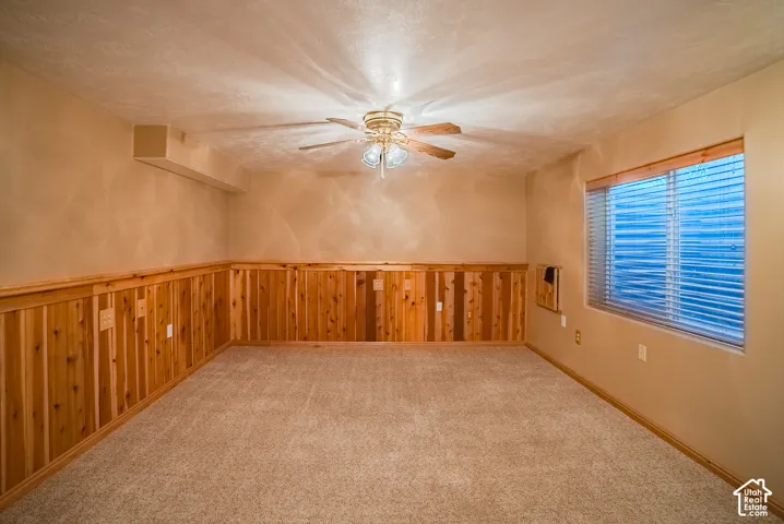 Room featuring wall-to-wall carpeting, wood-plank wainscoting, a ceiling fan with integrated lighting, and a window with horizontal blinds