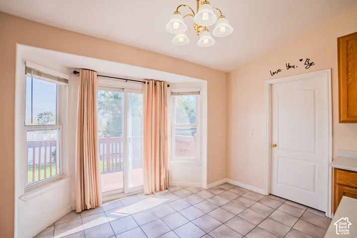 Bay window with sliding glass door access to exterior decking, ceramic tile flooring, five-light brass-finish chandelier, and solid-core interior door