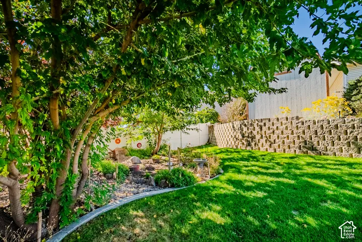 Backyard featuring a tiered stone retaining wall, mature trees, landscaped rock garden, and vinyl privacy fencing