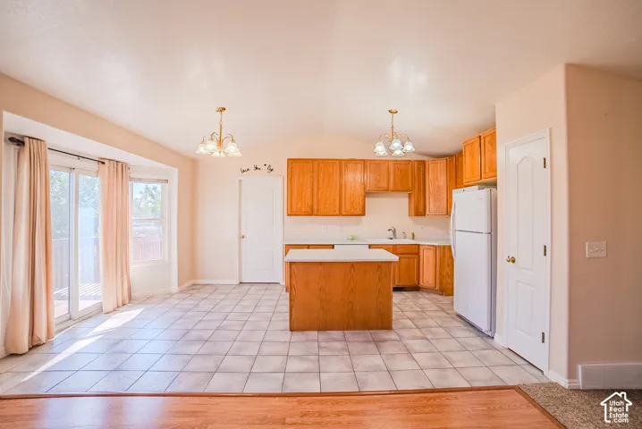 Kitchen featuring wood cabinetry, a central island, tile flooring, dual multi-bulb chandeliers, and glass sliding doors