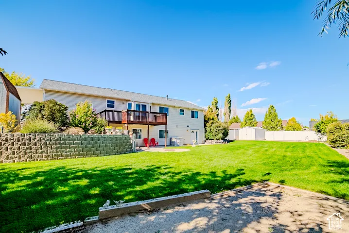 Expansive backyard featuring a tiered stone retaining wall, raised wooden deck, paved patio area, and mature landscaping