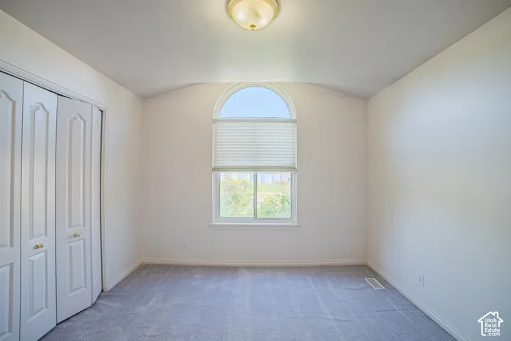Vaulted ceiling with an arched window, neutral wall palette, carpeting, and multi-panel bi-fold closet doors