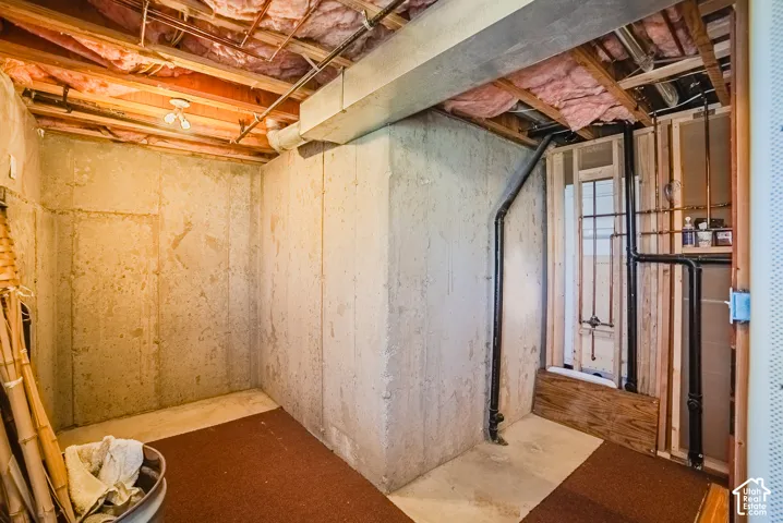 Unfinished utility space featuring poured concrete walls, exposed ceiling joists with insulation, and accessible plumbing systems