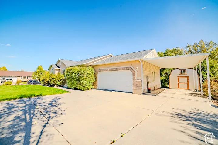 Exterior view featuring stucco and vinyl siding, an attached two-car garage with arched brick trim, a concrete driveway, a covered carport, and a detached storage shed