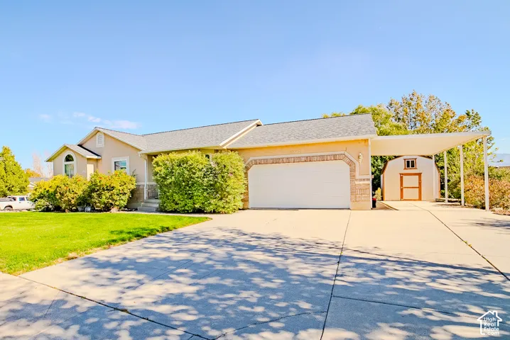 Single-story exterior featuring a stucco and brick facade, concrete driveway, attached two-car garage, and a detached carport with an auxiliary storage shed