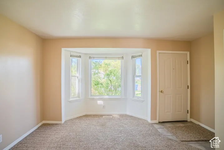 Neutral interior space featuring a large bay window, neutral-tone carpeting, and a solid-panel entry door