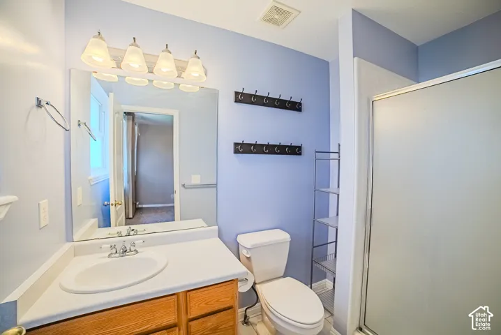 Bathroom featuring a wood-finish vanity with a molded countertop and integrated sink, a large wall-mounted mirror, four-bulb vanity lighting, and a glass-enclosed shower