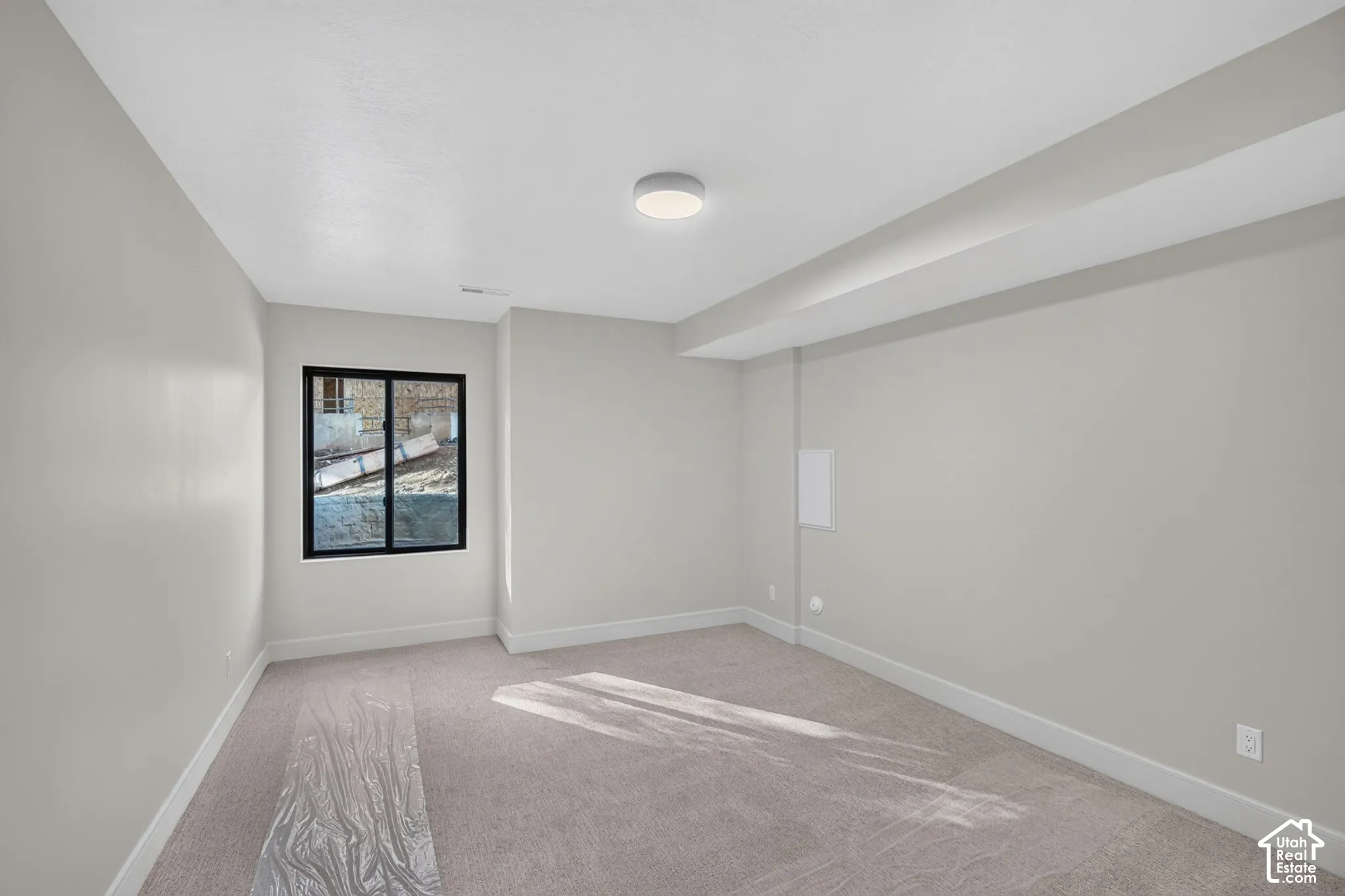 Interior room featuring neutral-toned carpeting, light-colored walls, a single-pane window with black trim, and a ceiling-mounted light fixture